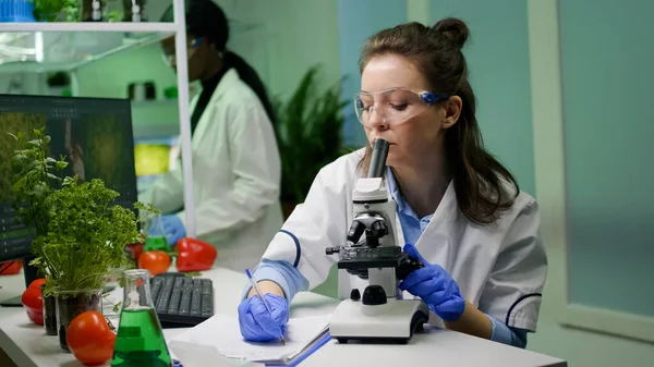 Biolog badający próbkę liści za pomocą mikroskopu medycznego — Zdjęcie stockowe