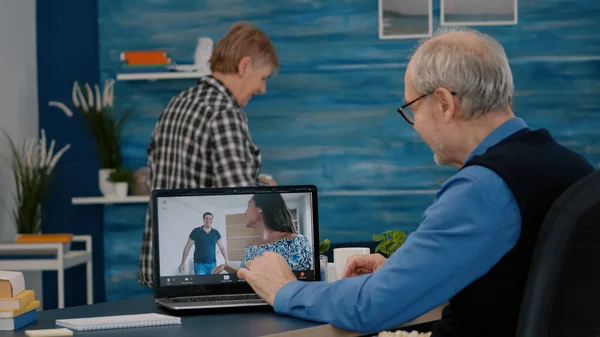 在与侄子们举行的视频会议上，快乐的老人一边用笔记本电脑一边挥手 — 图库照片