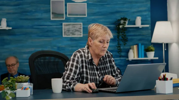 Ώριμη κυρία που εργάζεται σε φορητό υπολογιστή στο χώρο εργασίας πίνοντας καφέ — Φωτογραφία Αρχείου