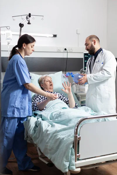 Medical team helping senior woman patient laying in hospital bed