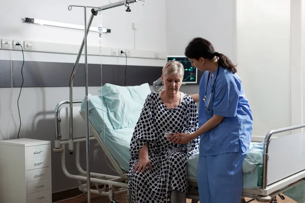 Önlüklü hemşire hastane odasındaki yaşlı kadına yardım ediyor. — Stok fotoğraf