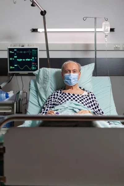 Portrét nemocného staršího pacienta s chirurgickou maskou spočívající v nemocničním lůžku — Stock fotografie