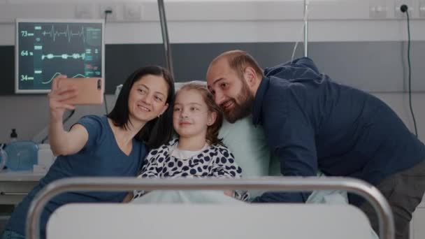 Familia positiva tomando selfie usando un smartphone moderno durante la consulta de enfermedades — Vídeo de stock