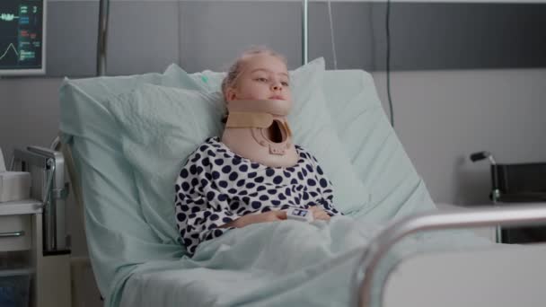 Portrét nemocného dětského pacienta ležícího v posteli a dívajícího se do kamery, zatímco má krční krční límec — Stock video