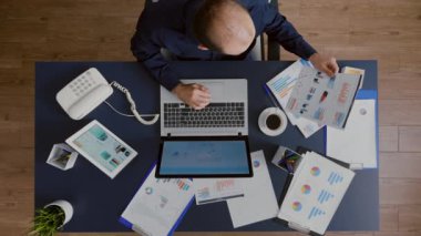 İşadamının yönetim grafiklerini analiz etmesinin üst görüşü şirket stratejisi fikirlerini belgelemektedir.