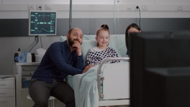 Patient malade hospitalisé allongé au lit avec sa famille regardant un film de divertissement à la télévision — Video