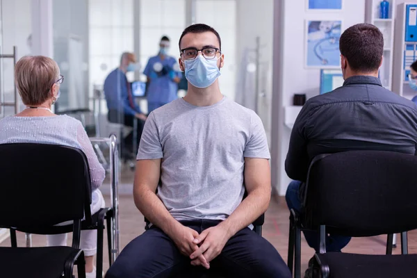 Yüzü maskeli yorgun bir adamın portresi bekleme salonunda oturmuş kameraya bakıyor. — Stok fotoğraf