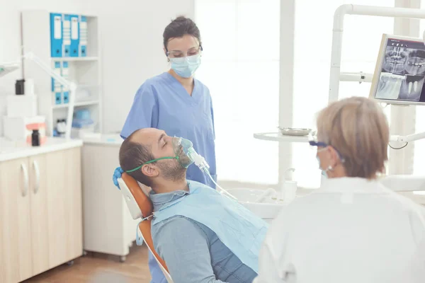 Zieke patiënt zittend op tandartsstoel met oxigen masker — Stockfoto