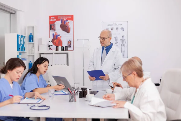 Fisioterapeuta hombre mayor discutiendo examen de enfermedad con el equipo médico — Foto de Stock