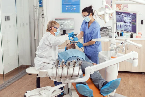 Врач-стоматолог и медсестра делают профессиональную чистку зубов больному человеку — стоковое фото