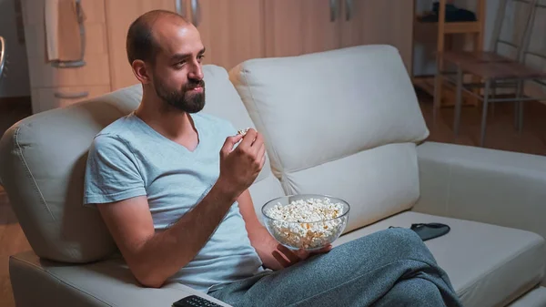 Caucasiano masculino refrigeração no sofá com pipoca tigela em mãos enquanto assiste série de filmes — Fotografia de Stock