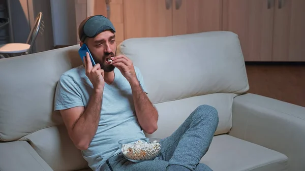 Caucasiano masculino descansando no sofá comendo pipocas enquanto falava ao telefone com um amigo — Fotografia de Stock