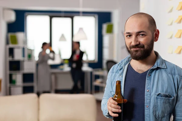 Caucásico hombre sonriendo y sosteniendo botella de cerveza después del trabajo —  Fotos de Stock