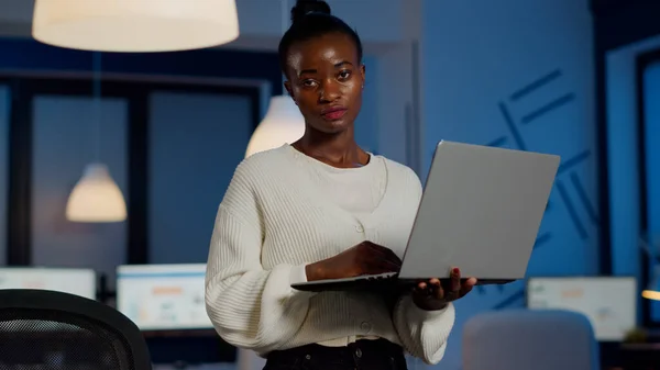 Exhausted business woman holding laptop, typing and sighing looking at camera