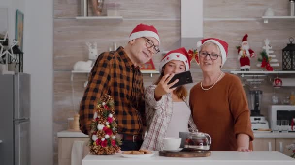 Avós felizes em pé à mesa em xmas cozinha decorada tirar selfie usando smartpgone — Vídeo de Stock