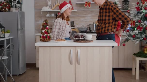 Familia feliz traer regalo de regalo de Navidad envoltura con cinta en ella en la cocina decorada con Navidad — Vídeos de Stock