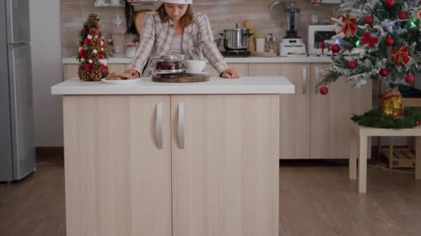 Retrato de menina vestindo chapéu de Papai Noel olhando para a câmera em pé à mesa em xmas cozinha decorada — Vídeo de Stock