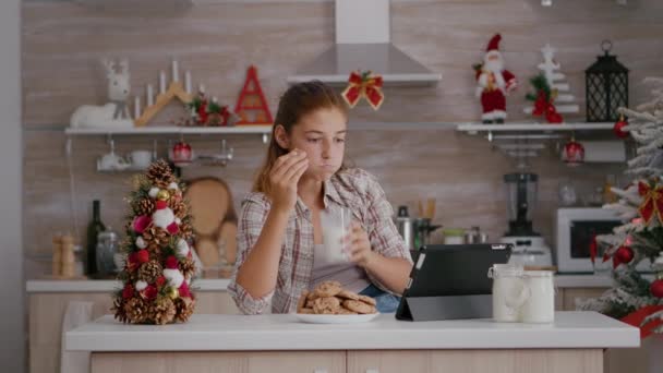 Porträtt av barn som äter bakade läckra kakor dricka mjölk medan du online xmas video på tablett — Stockvideo