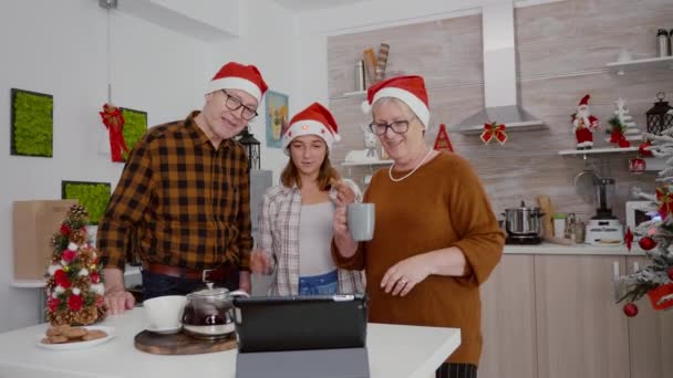 Famille heureuse portant santa chapeau tandis que debout dans la cuisine décorée de Noël saluant amis éloignés — Video