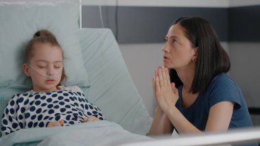 Hasta kız, ameliyattan sonra uyuyor. Anne de hastalık tedavisi için dua ediyor.
