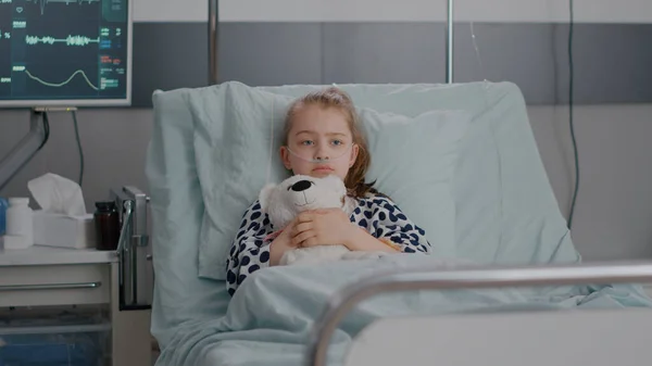 Portrait of lonley sick little child resting in bed holding teedy bear in hands — Stock Photo, Image