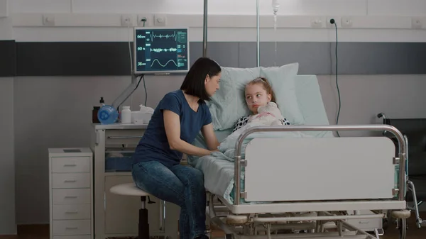 Bezorgde moeder zit naast zieke dochter tijdens ziekte-onderzoek in ziekenhuis afdeling — Stockfoto