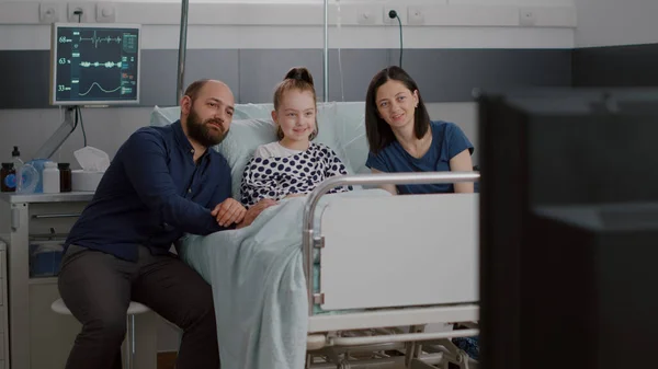 Ziekenhuisopname zieke kleine patiënt liggend in bed met familie kijken entertainment film op televisie — Stockfoto