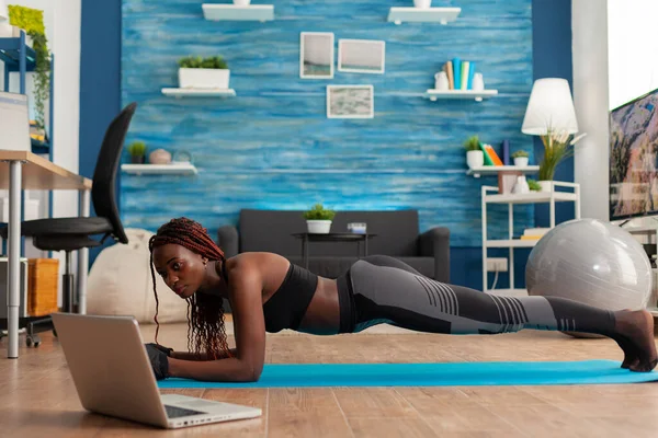 Спортсменка підходить чорна жінка в легінсах, сидячи на йога мат робить дошку позу — стокове фото