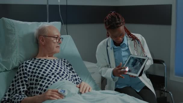 Afro-Amerikaanse arts toont röntgenfoto op tablet aan patiënt — Stockvideo