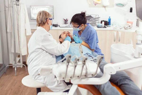 Больной пациент сидит в стоматологическом кресле с открытым ртом для осмотра — стоковое фото