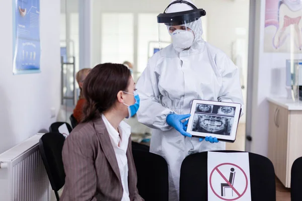 Stomatologist in protective suit pointing on digital x-ray of tooth