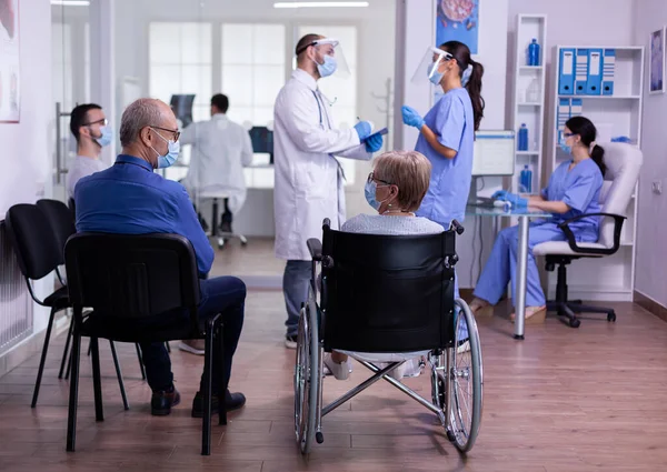 Médico especialista con visera y máscara de protección que habla con el asistente — Foto de Stock