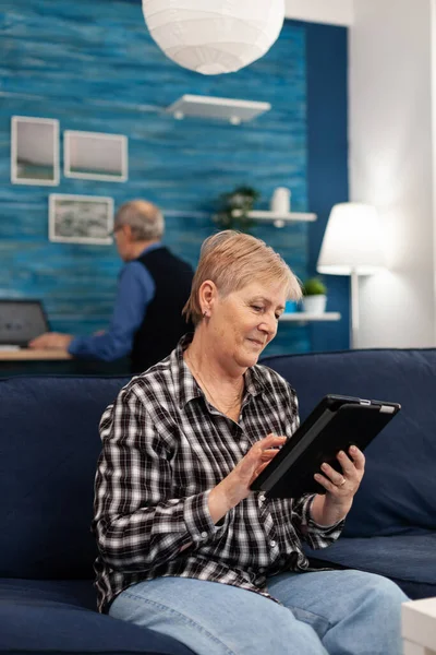 Donna anziana sorridente con tablet pc appoggiato sul divano — Foto Stock