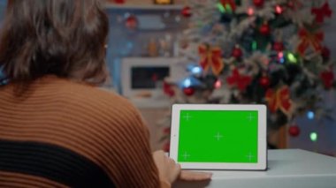 Genç bir kadın yeşil ekran ile evde oturuyor.