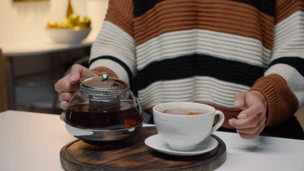 Женщина наливает чашку чая из чайника на кухонный стол — стоковое видео