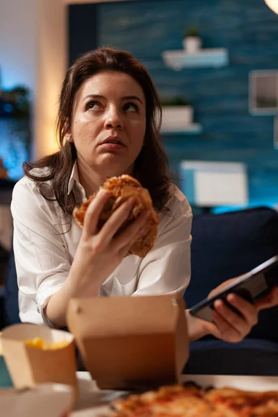 Caucasian female holding tastu burgery in hands browsing on social media using smartphone — Stock Photo, Image