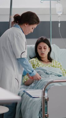 Pratisyen doktor yatağında dinlenen hasta kadını kontrol ediyor.