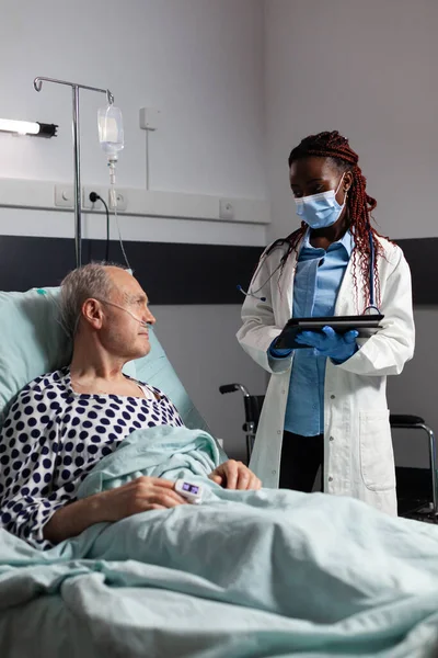 African american doctor with chirurgical mask in hospital room discussing diagnosis