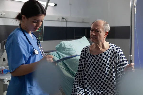 Старший больной мужчина в больничной палате обсуждает с медсестрой — стоковое фото