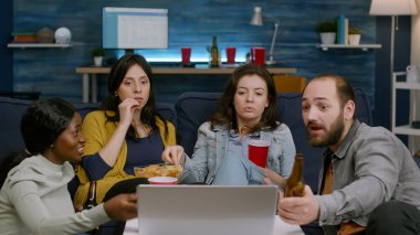 Kanepede oturup komedi filmi izleyen çok ırklı arkadaşlar.