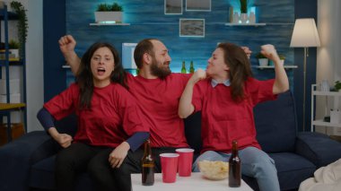 Coşkulu çoklu etnik arkadaşlar oturma odasında kanepede rahatlarken futbol takımını alkışlıyorlar.