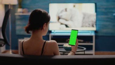 Elinde yeşil ekranlı cep telefonu tutan beyaz bir kadın.