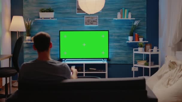 Jongeman zittend op de bank met groen scherm op tv — Stockvideo