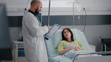 Afro-Amerikalı hemşire hastaların hastane koğuşunda rahat oturmasına yardım ediyor.