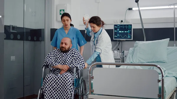 Medical team helping sick patient with leg fracture putting in wheelchair — Stock Photo, Image