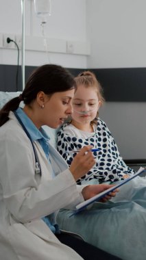 Annesi hasta küçük kızıyla tartışırken Afrikalı Amerikalı hemşire yatağı hazırlıyor.