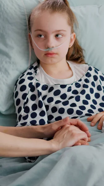 带氧气鼻管的住院儿童躺在床上，手上拿着医用血压计 — 图库照片
