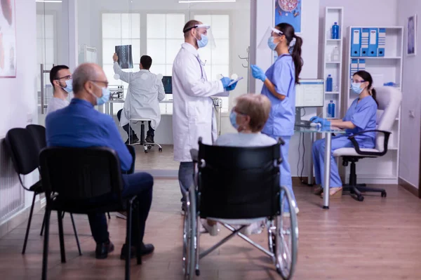 Equipo médico con visera y máscara de protección discutiendo de pie en la sala de espera — Foto de Stock