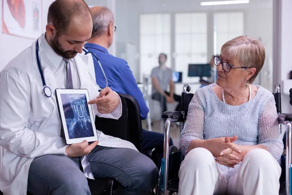 Médecin spécialiste montrant rayons X à la femme âgée en fauteuil roulant — Photo