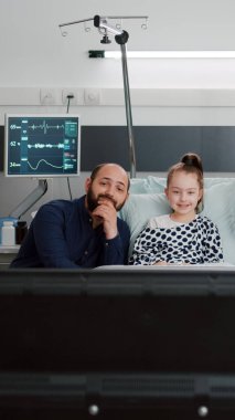 Hastanede yatan hasta bir çocuk ve ailesi televizyonda çizgi film seyrediyor.